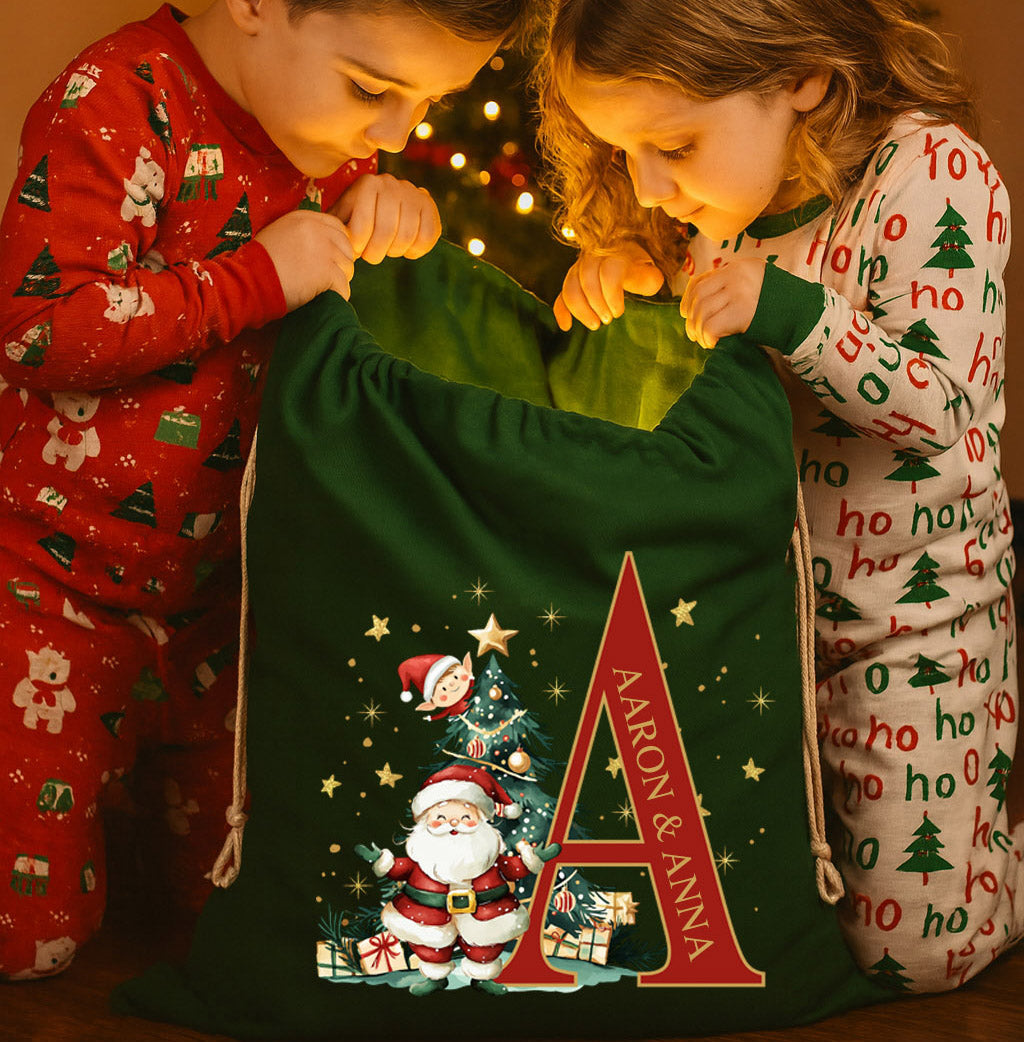 Two children in Christmas pajamas opening a green sack with Santa Claus and personalized initials.