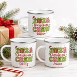 Three 2026 Christmas Crew personalised enamel mugs stacked with pine, candy canes and a gift