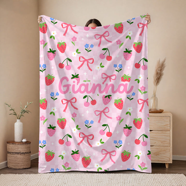 Person holding a pink blanket with strawberry and bow pattern in a room.