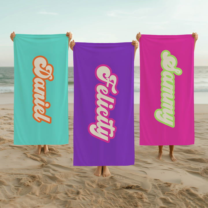 Three beach towels with personalized names held by people on a beach.